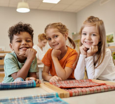 cheerful and multiethnic kids looking at camera near table in class of montessori school