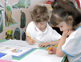 Two children sitting at a table, focused on their homework with books and pencils in front of them.